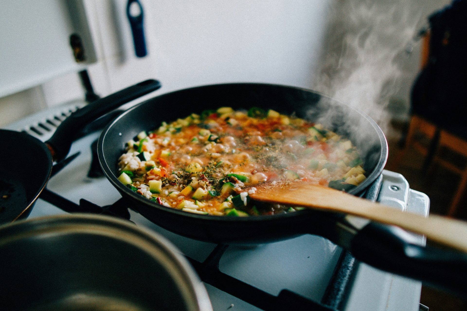 A pan of food cooking on a stove with a wooden spoon